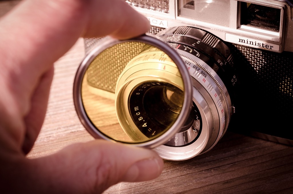 Eine Person hält eine gelbe Linse vor einer alten Kamera